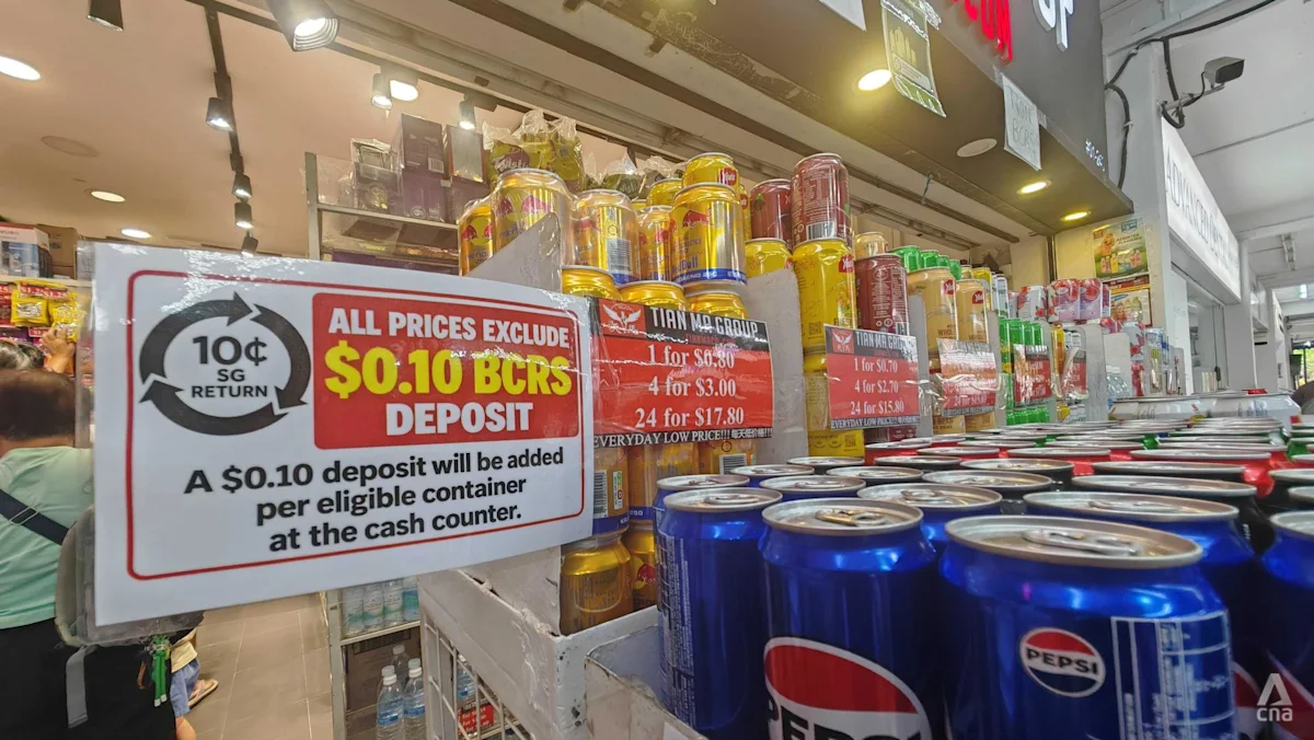 Pekerja ritel menempelkan stiker BCRS pada kaleng minuman di Singapura